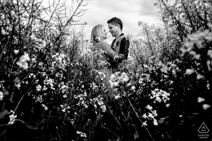 Auf diesem Schwarz-Weiß-Foto vor der Hochzeit eines Fotografen aus Aachen, Nordrhein-Westfalen blickt ein Paar einander an, während es in einer Blumenwiese steht.