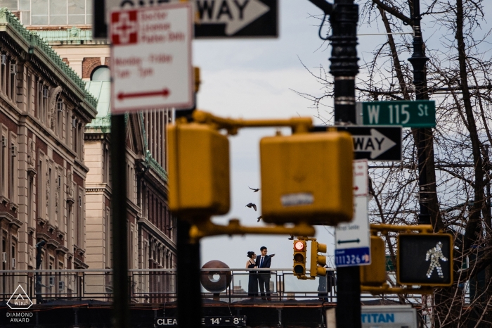 A couple can be seen through street signs as they stand outside of Columbia University in this pre-wedding photo by a New York City photographer.