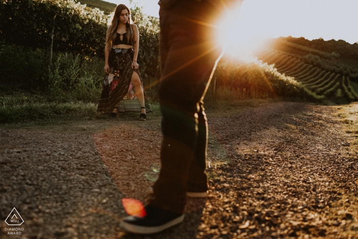 Photo by: <a href="https://www.wpja.com/photos/diamond-award-top-wedding-engagement-photographer/2495306">Renan Radici - Porto Alegre Rio Grande do Sul A couple stands on a dirt road in Bento Goncalves as the sun shines behind them during their engagement photoshoot by a Rio Grande do Sul, Brazil photographer.