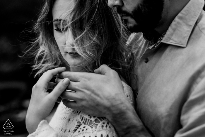 In Vitoria, a woman holds her fiance's hand as he stands behind her in this black and white pre-wedding portrait by a Rio Grande do Sul, Brazil photographer.