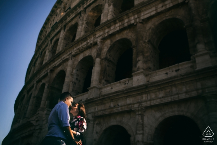Zdjęcie: <a href="https://www.wpja.com/photos/diamond-award-top-wedding-engagement-photographer/2496271"> Paolo Ferrera - Alvito Frosinone Para razem stoją i dotykają nosów przed rzymskim Koloseum podczas sesji zaręczynowej fotografa z Lazio, włoskiego fotografa.