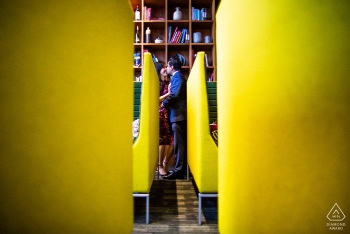 On voit un couple s'embrasser à travers une rangée de bancs jaunes dans ce portrait de fiançailles réalisé par un photographe de San Francisco, Californie.