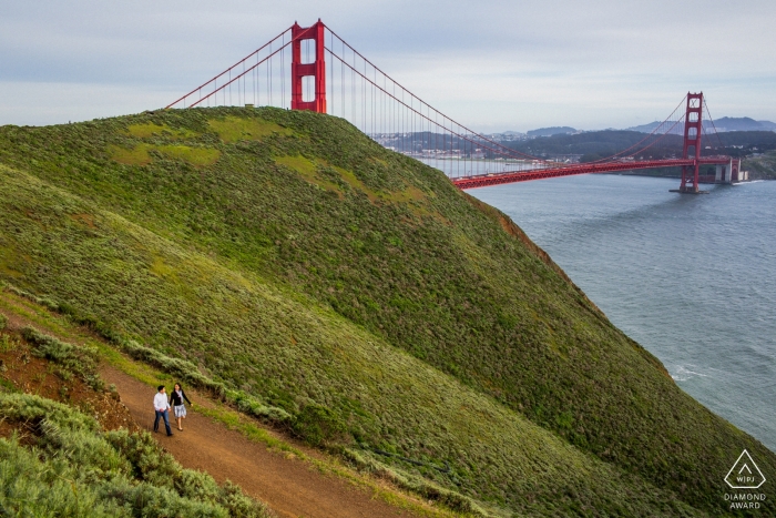 Un couple se promène sur un chemin de terre près du Golden Gate Bridge de San Francisco lors de cette séance de fiançailles avec un photographe californien.