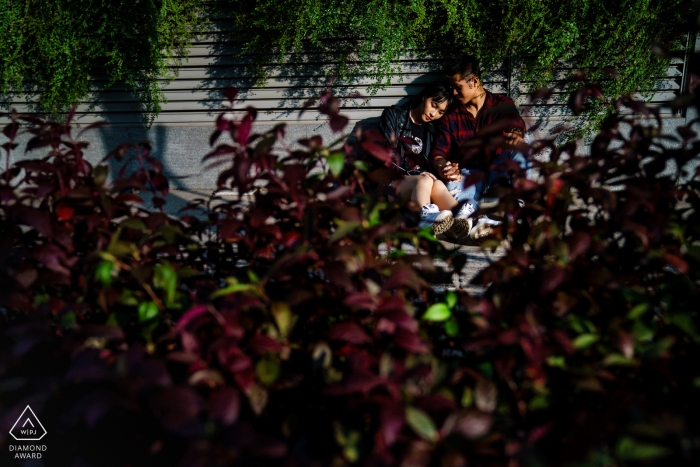 Photo by: <a href="https://www.wpja.com/photos/diamond-award-top-wedding-engagement-photographer/2496756">Vu Nguyen - Ho Chi Minh A couple sits together in Saigon partially hidden behind a bush in this pre-wedding photo by a Ho Chi Minh, Vietnam photographer.
