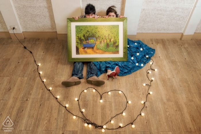 Photo by: <a href="https://www.wpja.com/photos/diamond-award-top-wedding-engagement-photographer/2497401">Tao-Hsuan Tzu - Ji’an Township, Hualien County A couple sits on the floor holding a painting while a string of lights shaped into a heart lays on the floor in front of them for their pre-wedding photoshoot by a Hualien County, Taiwan photographer.