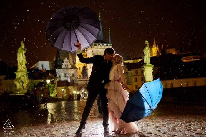 During a torrential downpour this Engaged couple share a kiss  in Prague during their evening engagement session at the Charles Bridge