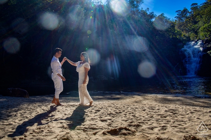 Ein Mann zieht seinen Verlobten näher an sich heran, als sie während ihres Verlobungsfotoshoots eines Fotografen aus Goias, Brasilien, im Sonnenlicht von Pirenopolis über den Sand gehen.