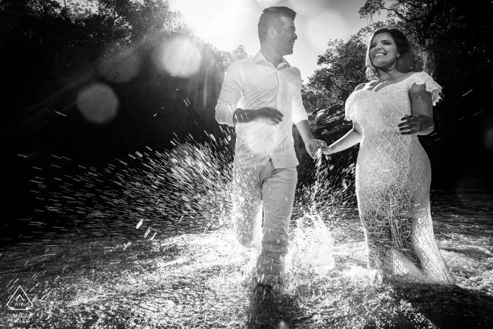 Un couple traverse l'eau à Pirenopolis alors qu'ils se tiennent la main dans ce portrait de mariage en noir et blanc réalisé par un photographe de Goias, au Brésil.