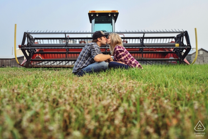 Un couple est assis dans l'herbe et embrasse devant un tracteur dans cette photo prise avant le mariage par un photographe de l'Alberta, au Canada.