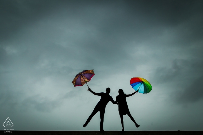 Photo by: <a href="https://www.wpja.com/photos/diamond-award-top-wedding-engagement-photographer/2500451">Anupa Shah - Mumbai Maharashtra The silhouettes of the couple holding bright umbrellas against a gray sky was captured by a Mumbai engagement photographer