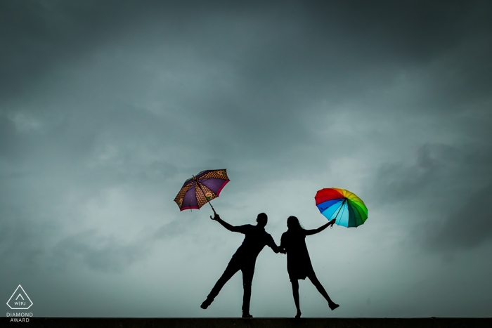 The silhouettes of the couple holding bright umbrellas against a gray sky was captured by a Mumbai engagement photographer 