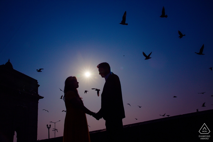 Les silhouettes du couple se tiennent par la main pendant que les oiseaux volent autour d'eux lors de leur session pré-mariage à Bombay