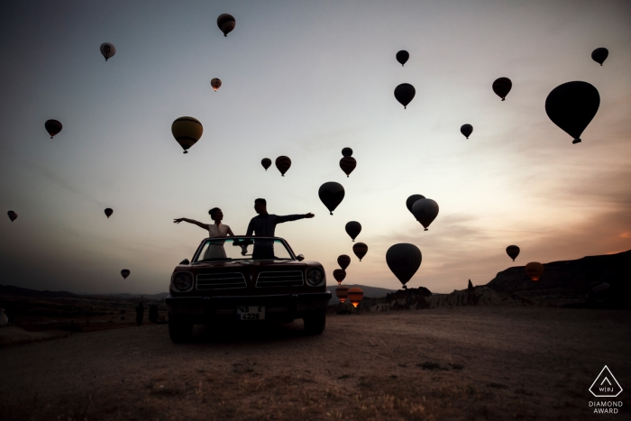 Sihouetted air balloons fly around the enagged couple during their pre-wedding session in Turkey, Cappadocia