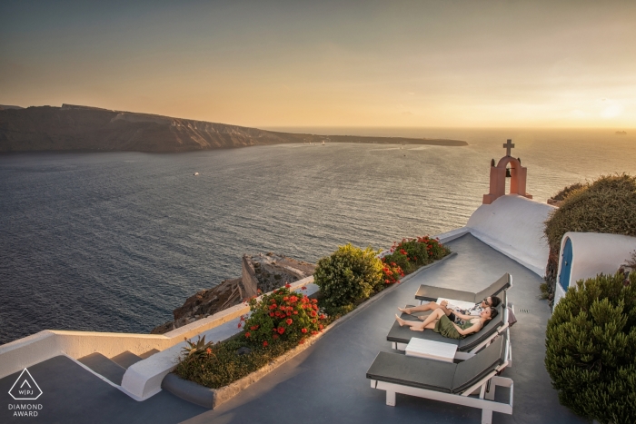 Este casal de noivos relaxar ao lado da água ao pôr do sol durante seu ensaio de noivado em Santorini