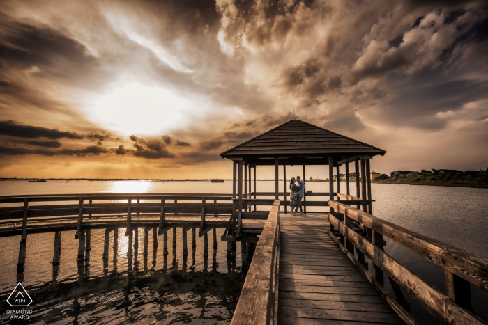 Photo by: <a href="https://www.wpja.com/photos/diamond-award-top-wedding-engagement-photographer/2502981">Luca Fabbian - Schio Vicenza A Venice engagement photographer caught this photo of a couple embracing on a pier at sunset near Porto Caleri