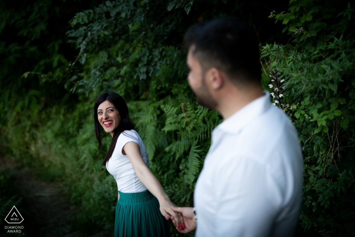 The soon to be bride smiles back at the groom as they walk hand in hand down a path near Rovaglio-Palmi in this photo shot by a Calabria engagement photographer The soon to be bride smiles back at the groom as they walk hand in hand down a path near Rovaglio-Palmi in this photo shot by a Calabria engagement photographer