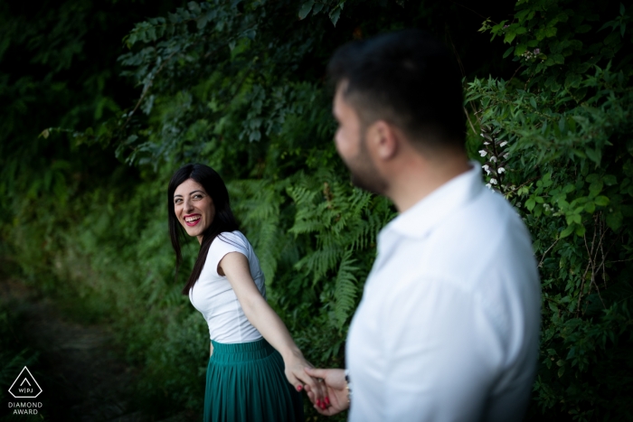 Die Braut, die bald heiraten wird, lächelt dem Bräutigam zu, als sie auf diesem Foto, das von einem Verlobungsfotografen aus Kalabrien aufgenommen wurde, Hand in Hand einen Weg in der Nähe von Rovaglio-Palmi entlanggehen