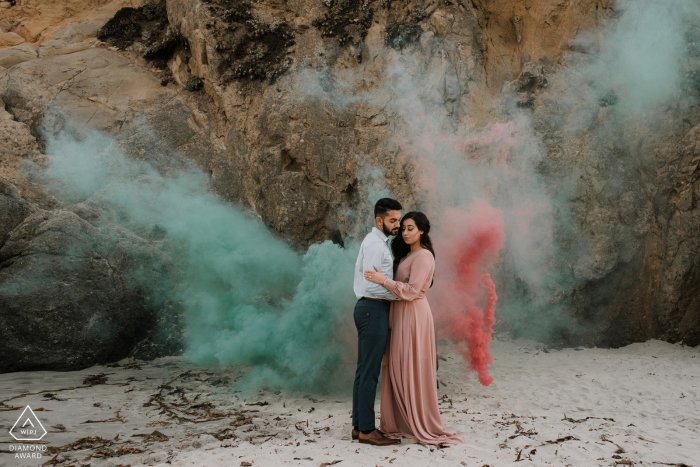 Retrato de compromiso de boda de CA en la arena de la playa con humo de colores.