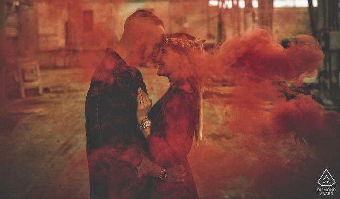 Liguria engagement photographer designed this portrait of a couple embracing while shrouded in red smoke in Bolano