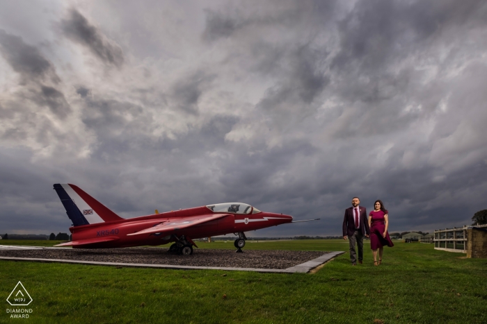 Paar-Verlobungsporträt mit rotem Kleid und rotem Flugzeug am Flughafen Cotswald, Großbritannien