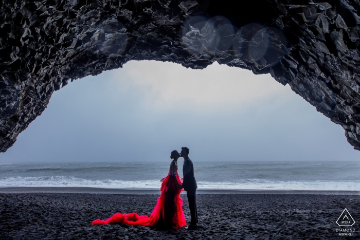 Fotos de la boda previa a la isla en la playa con cueva de arco y vestido rojo