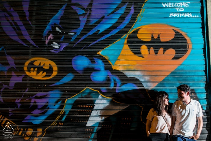 Athens, Greece Engagement Photos - Couple looking each other in front a big Batman mural