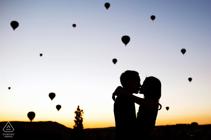 Verlobungsphotograph Cappodocia, die Türkei, der einen Kuss bei einem magischen Sonnenaufgang mit Ballonen gefangennimmt