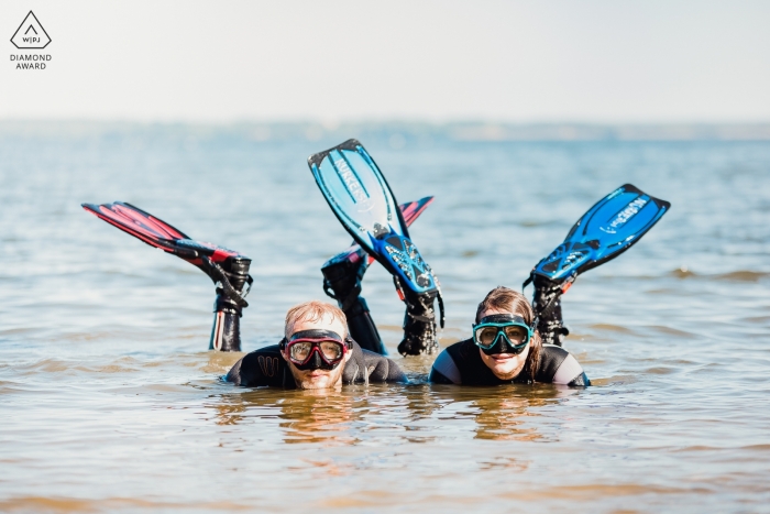 Foto de noivado Popowo Beach de um casal deitado na água com óculos e barbatanas.