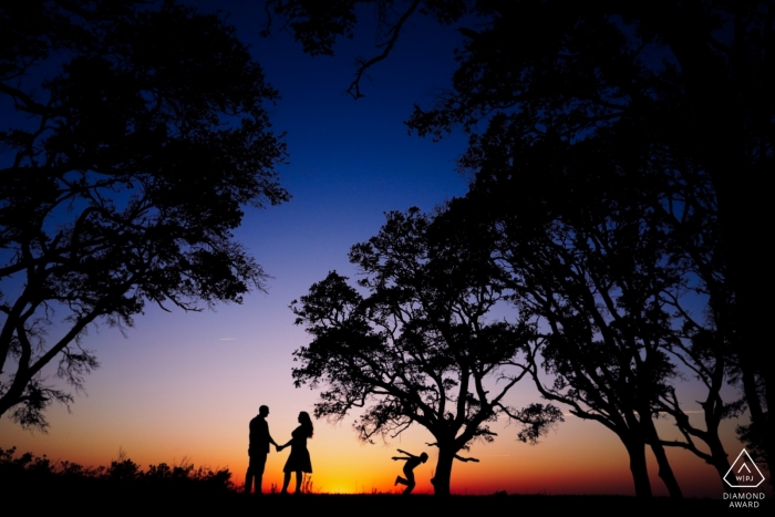 Foto di: <a href="https://www.wpja.com/photos/diamond-award-top-wedding-engagement-photographer/2544104"> Joe Payne - Raleigh North Carolina Fort Fisher, North Carolina Couple Portraits - Foto di fidanzamento delle future coppie con il figlio della sposa che corre in silhouette
