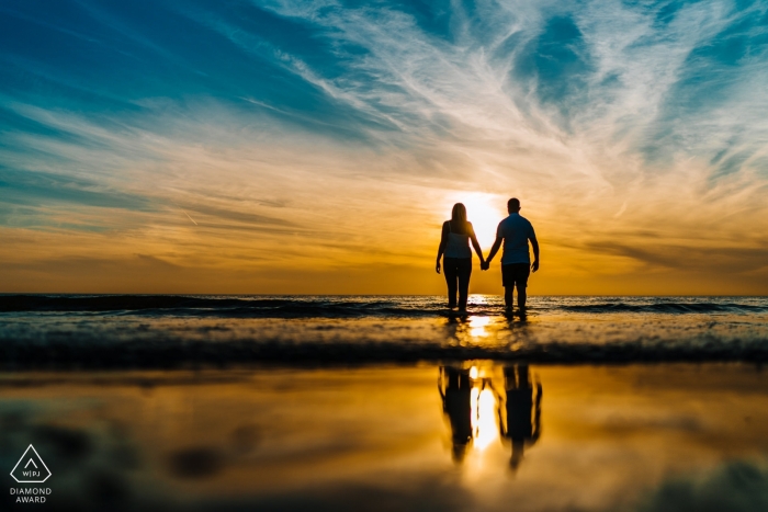 Sessione di fidanzamento al tramonto sulla spiaggia in Inghilterra con riflessione di coppia nell'acqua