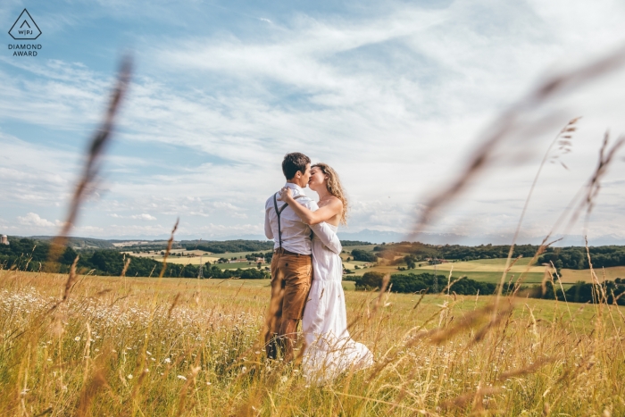 Foto von: <a href="https://www.wpja.com/photos/diamond-award-top-wedding-engagement-photographer/2546869"> Isabelle Bazin - Goutz Marciac, Frankreich | Ein Paar, das in einer Landschaft während der Verlobungsfotosession im Gras küsst