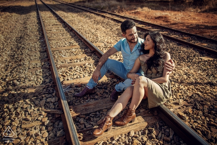 Sessão de retratos pré-casamento no Brasil com casal sentado em trilhos de trem.