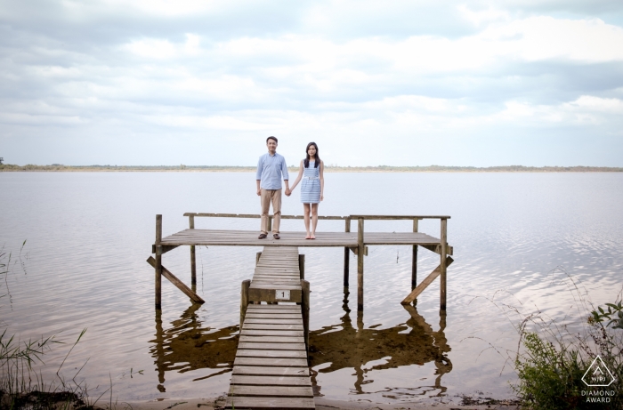 A couple on a pier looking at the camera during engagement portrait shoot at Lacanau, south west of France