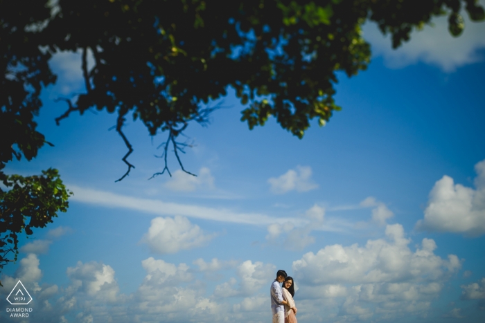 Verlobungsfotos - Bali Paar bei Sonnenuntergang mit Wolken, blauem Himmel und Bäumen.