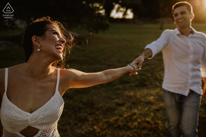 Engagement Portrait from O Butia - Porto Alegre - Rio Grande do Sul - Photography contains: couple, hands, grass, trees, park, laughing