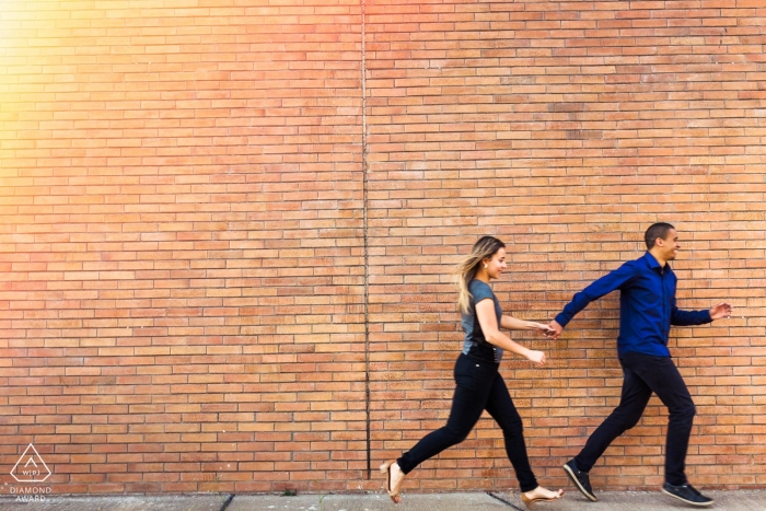 Vicosa Brazil Couple running together during prewedding portrait shoot against a brick wall.