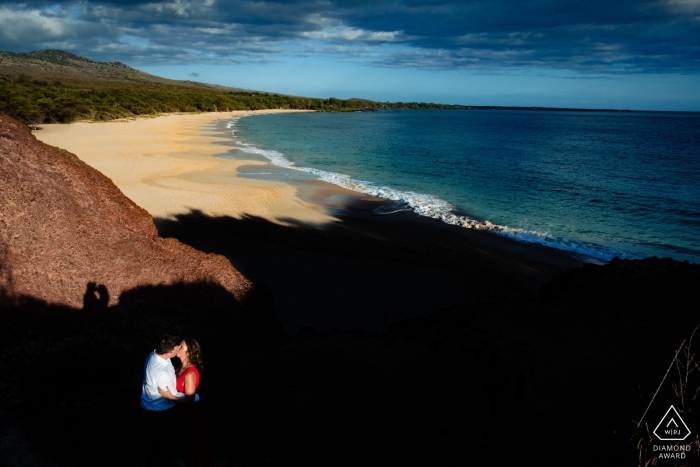 Photo by: <a href="https://www.wpja.com/photos/diamond-award-top-wedding-engagement-photographer/2558133">Angela Nelson - Makawao Hawaii Engaged couple kissing in the hardlight above the beach at Wailea, Maui, Hawaii