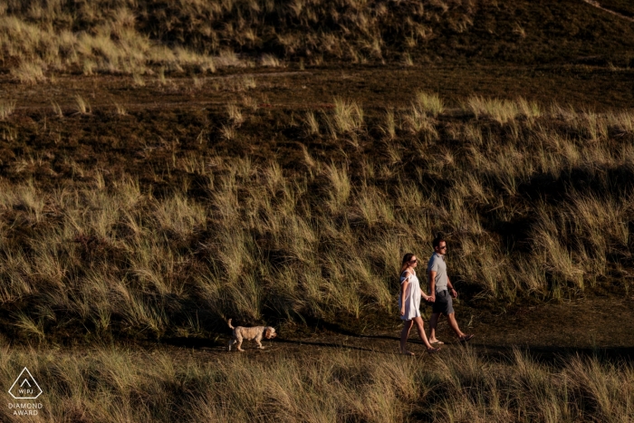Photo by: <a href="https://www.wpja.com/photos/diamond-award-top-wedding-engagement-photographer/2559354">Catherine Hill - Canterbury Kent The Sand Dunes, St Ouen, Jersey, Channel Islands Engagement Photos | The couple brought their dog along for their engagement shoot. I wanted to include the colours and textures of the landscape - their dog was amusing following on behind!