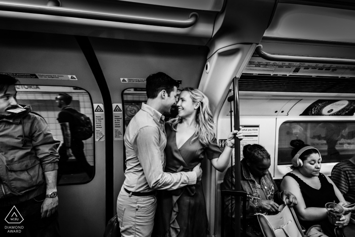 Photo by: <a href="https://www.wpja.com/photos/diamond-award-top-wedding-engagement-photographer/2560025">Paul Tansley - Bordon Hampshire Victoria Tube Station, London — Couple on the Victoria Line Tube, hugging, while other passengers go on about their business, train is pulling away from platform - BW image