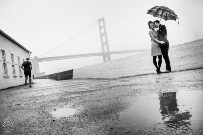 Photographe de mariage et de fiançailles à San Francisco - Étreinte sous la pluie. Couple avec parasol et flaques.