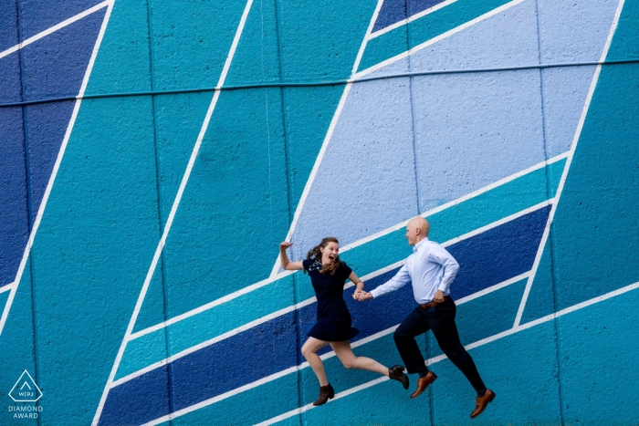 Photo by: <a href="https://www.wpja.com/photos/diamond-award-top-wedding-engagement-photographer/2560127">Brittany Diliberto - Arlington Virginia Crystal City, VA A couple jumps enthusiastically in front of a blue toned mural. Engagement photo session with fine art.