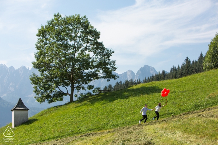 Gosau engagement session of a couple running through the Austrian mountains with red balloons Gosau engagement session of a couple running through the Austrian mountains with red balloons