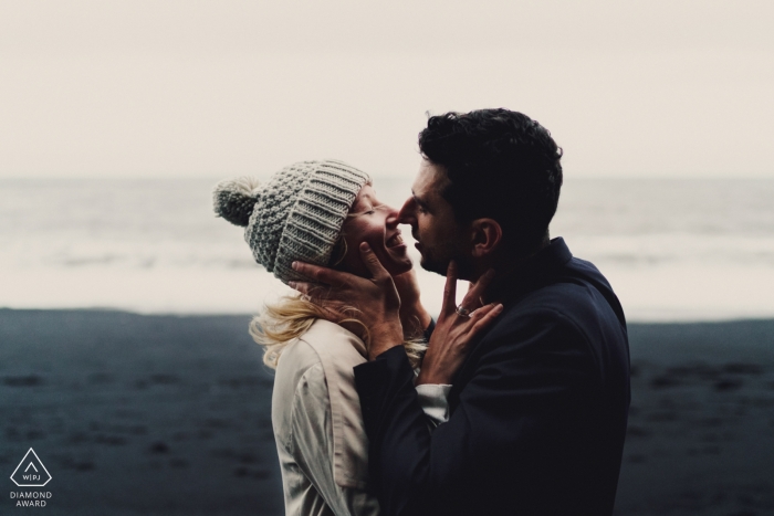 Pareja en la playa de arenas negras besándose durante la sesión de retratos de compromiso en Islandia