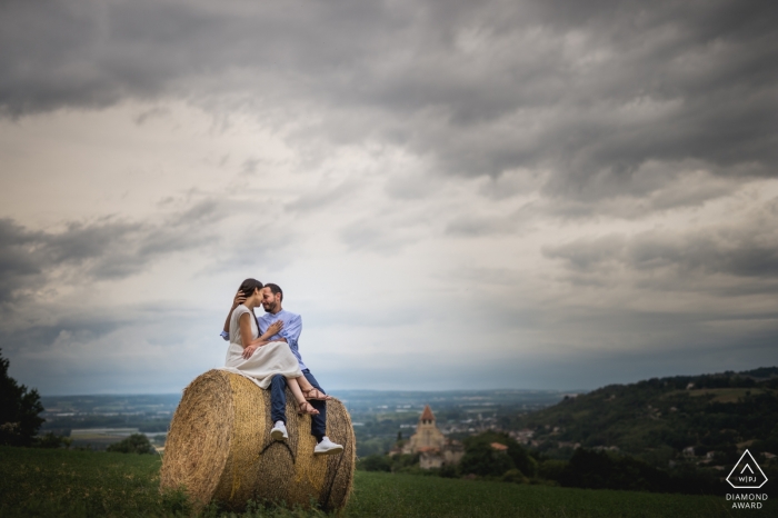 Autor zdjęcia: <a href="https://www.wpja.com/photos/diamond-award-top-wedding-engagement-photographer/2562771"> Franck Petit - Serignac sur Garonne Agen, Francja para portret w polu siedzi na okrągłej beli siana.