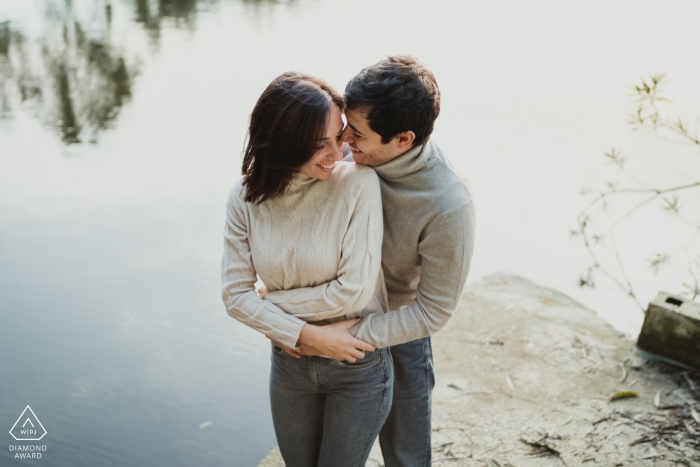 Engagement in Naples photograph of an engaged couple holding each other standing on rock by the water.