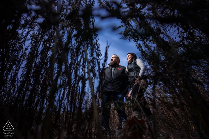 Sesión de compromiso de Minnesota en Silverwood Park - Pareja en la hierba alta con un cielo azul detrás de ellos