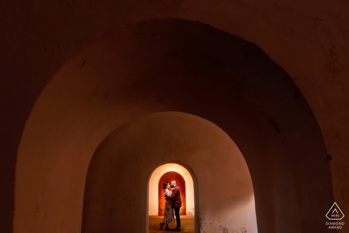 El Morro, San Juan PR Engagement Portrait d'un couple - L'image contient: Encadrement du couple avec les arcades et la porte derrière le couple.