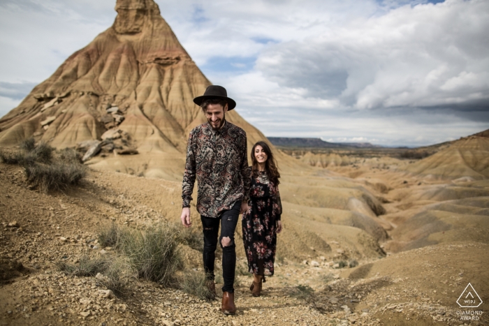 Gironda dois amantes caminhando no deserto - Foto de noivado de um casal - Retrato contém: areia, terra, caminhada, montanha, chapéu