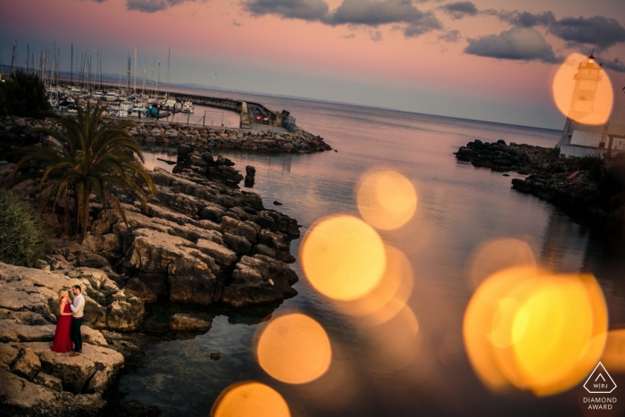 Sessão do Farol de Cascais - Retrato de noivado de um casal - Imagem contendo: bokeh, pedras, água, praia, enseada, vestido vermelho