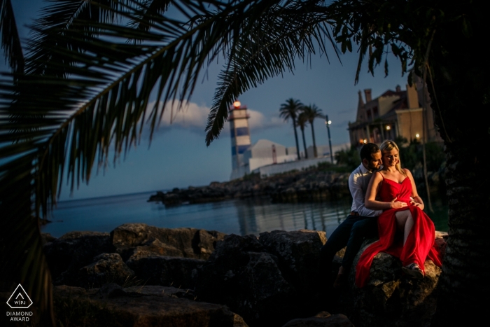 Cascais, Portugal Engagement Photo of a Couple - Portrait contains: last light, red dress, palm trees, blue sky